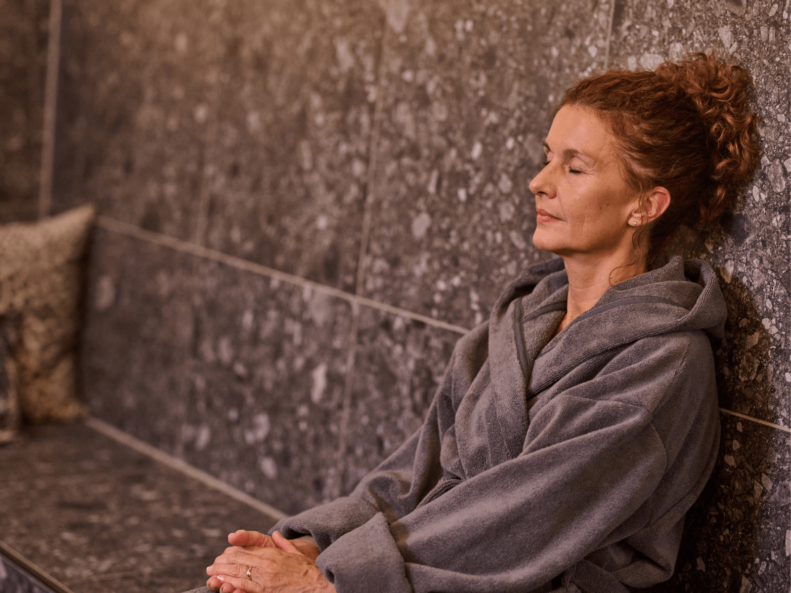 Attraktives weibliches INJOY Mitglied sitzt mit geschlossenen Augen im INJOY Erholungsbereich.